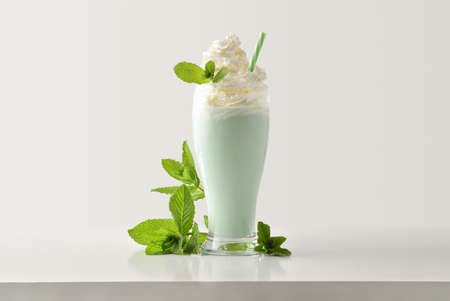 Mint milkshake with cream decorated with leaves around on white wooden table and light isolated background. Front view.の写真素材