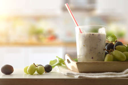 Organic liquid grape yogurt on white plate with bunches of white and red grapes in try on wooden table with kitchen background. Front view.の写真素材