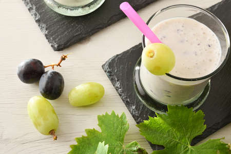 Organic grape yogurt on slate plate with bunches of white and red grapes on wooden table. Top view.の写真素材