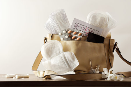Purse with various menstrual hygiene products for women on wooden table. Front view.