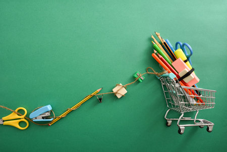 Shopping concept with shopping cart with school supplies on top and pulling tools hooked to a rope...