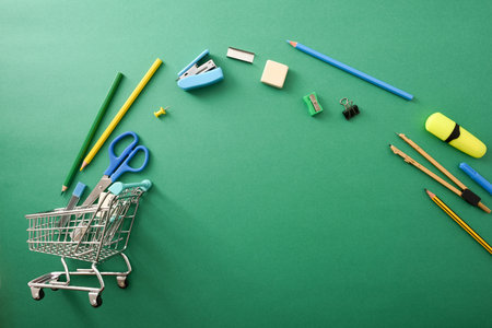School supplies shopping concept with tools coming out of shopping cart sliding on a green table....