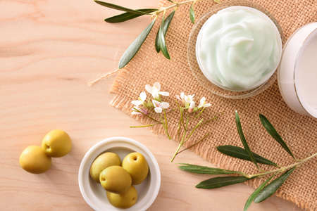 Moisturizing cosmetic cream with olive extract for skin with branch and olives on wood table. Top view.の写真素材
