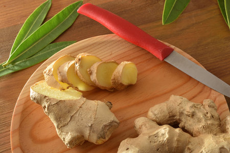 Ginger root slice on wooden cutting board on wooden table with leaves. Top elevated view.の写真素材