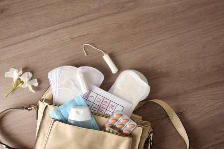 Purse with various menstrual hygiene products and covid-19 protection for women on wooden table. Top view.の写真素材