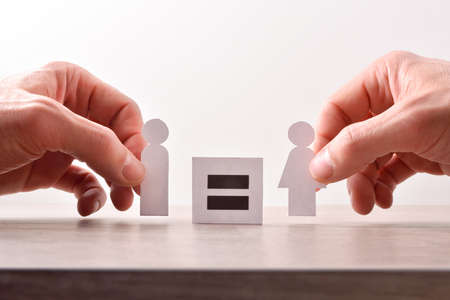 Gender equality concept with hands catching cutouts shaped like man and woman holding sign with equal signの写真素材