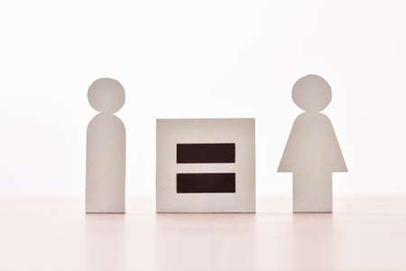Equality between man and woman with equal sign between two paper cutouts shaped like man and woman on wooden table.の写真素材