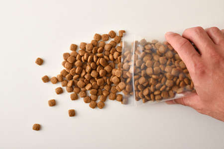Man's hand dropping dog kibble from a clear plastic bag onto a white table. Top view. Horizontal composition.の写真素材