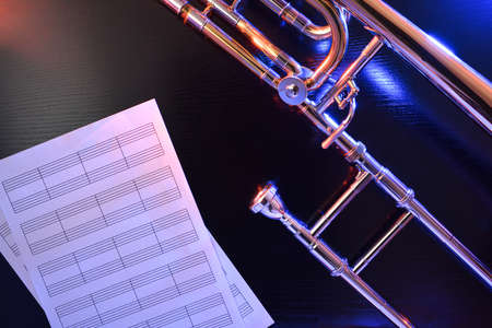Jazz trombone with empty staff sheets illuminated with colored lights on black table. Top view. Horizontal composition.の写真素材