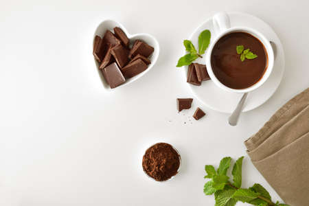 Hot chocolate in white ceramic mug, pieces in heart-shaped bowl and chocolate powder in bowl on white table. Top view. Horizontal composition.の写真素材