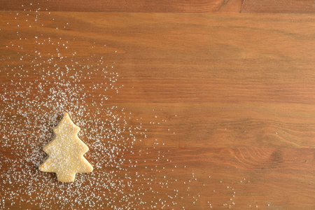 Christmas background with fir-shaped cookie in one corner sprinkled with icing sugar on wooden...
