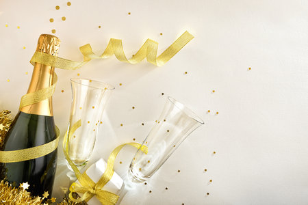 New year's eve party celebration background with sparkling wine bottle and glasses to bundle with confetti gift ribbons and golden decoration on white table. Top viewの写真素材