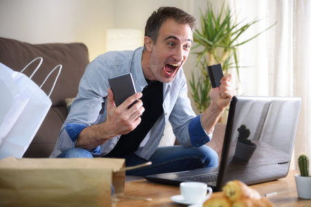 Excited man making excellent online purchase with credit card in hand and moil, looking at laptop in...