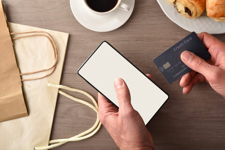 Making an internet purchase from home from a smartphone on the kitchen bench with breakfast. Top...