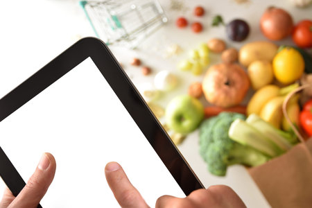 Finger pressing mobile device screen to place shopping order in supermarket with shopping bag and...