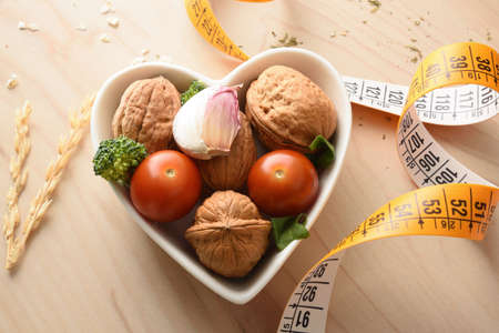 Healthy eating weight control concept with fruits and vegetables in heart shaped bowl and measuring tape on wood table detail. Top view. Horizontal composition.の写真素材