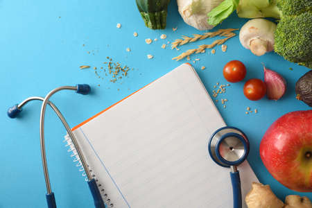 Health care guidelines with natural balanced food with fruits and vegetables and notepad with blank sheet on blue table. Top view. Horizontal composition.の写真素材