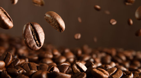 Roasted hot coffee beans falling on pile of coffee beans. Frontview. Landscape composition.