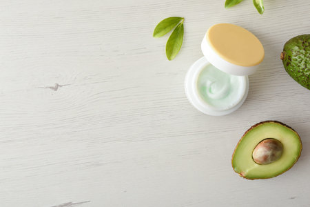 Natural moisturizing cream with avocado extract for skin care with fruits and leaves on white table....