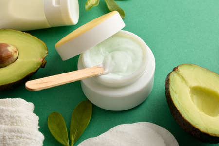 Moisturizing cream and lotion with avocado extract for skin care with fruit and toiletries on green table close up. Elevated view. Landscape composition.の写真素材