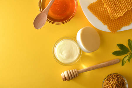 Moisturizing skin care cream with honey extracts with pot and plate with honeycombs and pollen on yellow table. Landscape composition. Top view.の写真素材
