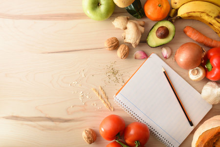 Vegetables on a wooden table and open notepad with empty leaf and pencil to score. Top view....