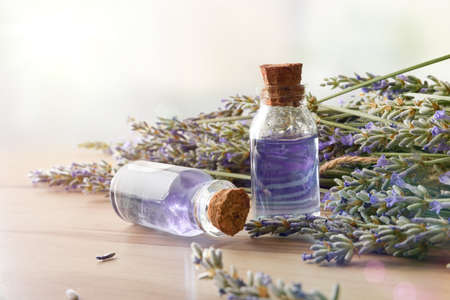 Two glass bottles with lavender extract on wooden table with bunch of spikes around.. Front view. Landscape composition.の写真素材