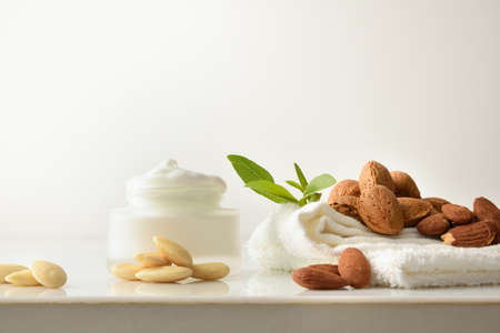 Almond moisturizing cream skin care with fruits towel and leaves on white table and white isolated background. Frontview. Landscape composition.の写真素材