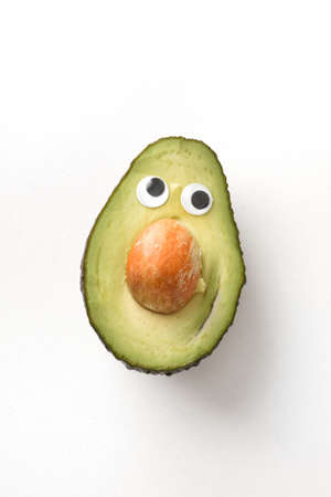 Fresh funny avocado inside with face on white isolated background. Fruit child healthy eating conceptの写真素材