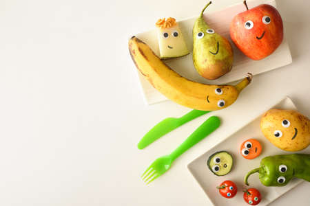 Background with plate of funny fruits with drawn eyes and mouths served for children on white table. Top view.の写真素材