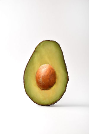 Detail of half ripe avocado showing the central bone isolated on white table. Frontview; Vertical...