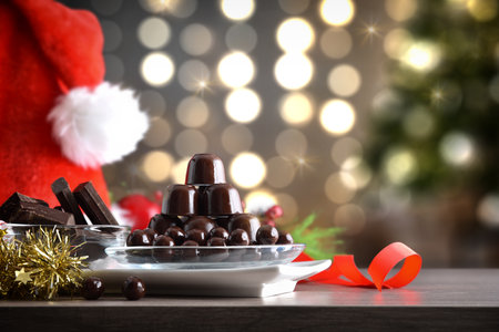 Plate with stack of chocolates and dark chocolate balls on wooden table with Christmas decoration and christmas background with lights. Front view.の写真素材