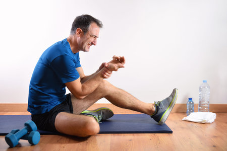 Man doing sports indoors complaining of wrist pain sitting on a mat. side view