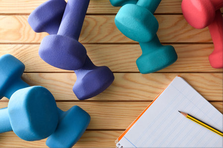 Training plan for bodybuilding exercises with notepad and dumbbells on wooden table. top view.の写真素材