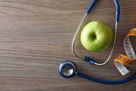 Health check and healthy lifestyle with apple, tape measure and stethoscope on wooden table. top view.の写真素材