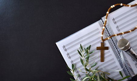 Choral music background for Palm Sunday with sheet music, microphone and olive branches with a Christian cross on a black table. top view.の写真素材