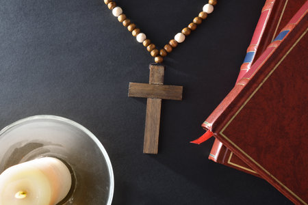 Black bedside table with religious elements to pray with a Christian cross Bible and a lit candle on a glass plate. top view.の写真素材