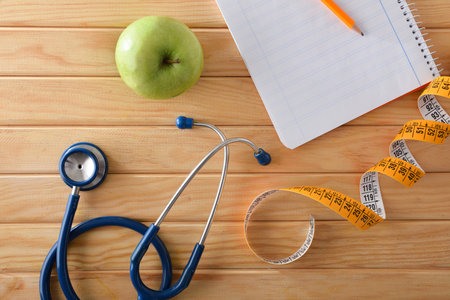 Body control and healthy plan with notebook and pencil on wooden table with apple, tape measure and stethoscope. top view.の写真素材