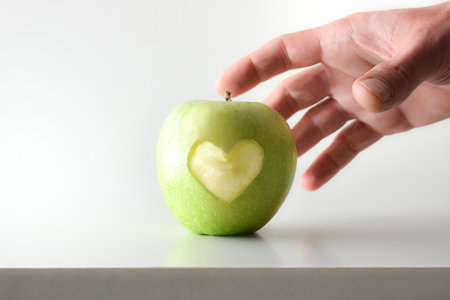 Hand picking apple with heart on white table and white isolated background. Front view.の写真素材