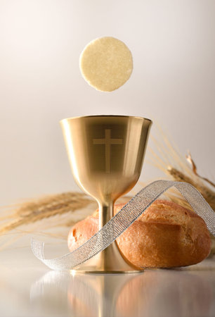 Reminder of the first communion with a chalice cup with an engraved cross and a host on a table with...