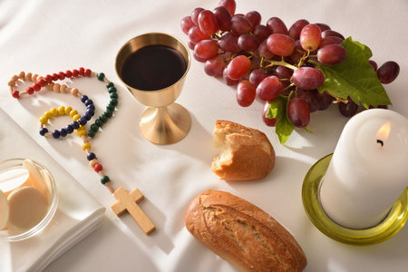 Eucharistic elements such as wine, bread and bunch of grapes on a table with a white tablecloth with a Catholic cross and a lit candle. Elevated view.の写真素材