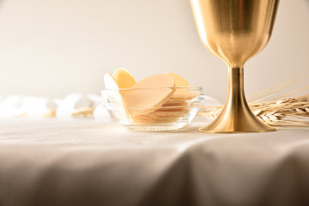 Detail of cup and hosts in glass container on table with white tablecloth and ears of wheat behind with white isolated background.. Front view.の写真素材