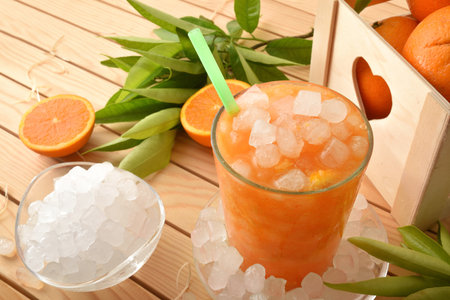 Glass with natural orange drink with a lot of ice and basket with fruit on a wooden table. Elevated view. Horizontal composition.の写真素材