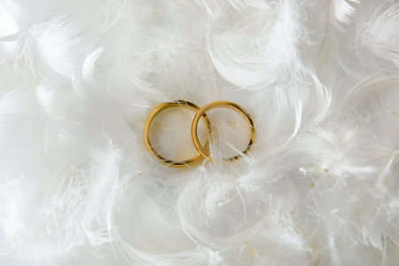 Detail of two gold rings on white table with white feathers around. top view.
