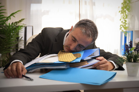 Businessman asleep from exhaustion on a pile of folders and documents on the desk in the officeの写真素材