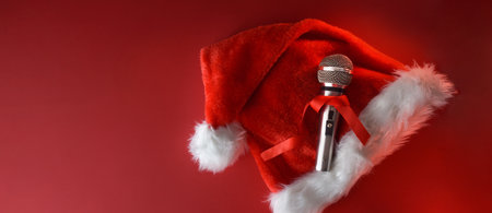 Christmas musical background with metallic stage microphone with red bow on santa hat isolated on red background. Top view.の写真素材