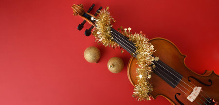 Violin with a red background decorated with tinsel and golden Christmas balls. Top view.