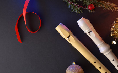Two traditional plastic recorders for children's music events on a black table with Christmas...
