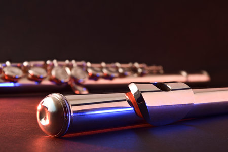 Detail of metal flute head and body in the background on black table with red and blue lights and...
