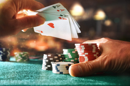 Hand with set of aces and betting chips on green gaming mat on table in gaming room. Front view.